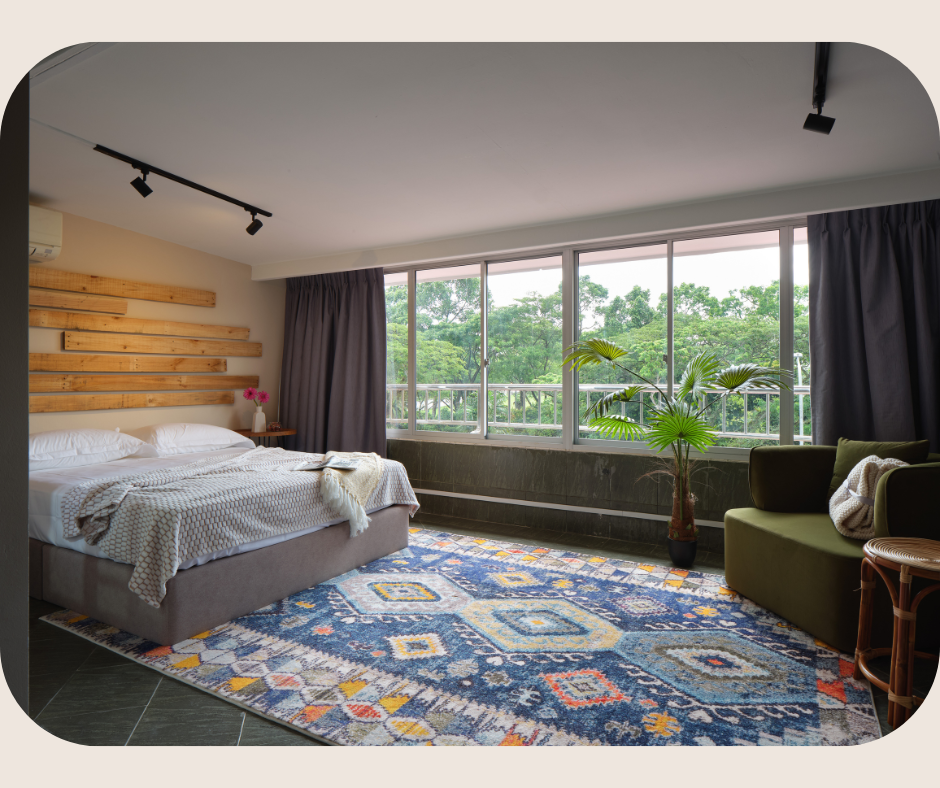 Bright, modern bedroom with large windows overlooking lush greenery, featuring a wooden headboard, patterned rug, and cozy seating, showcasing Living in Bukit Timah