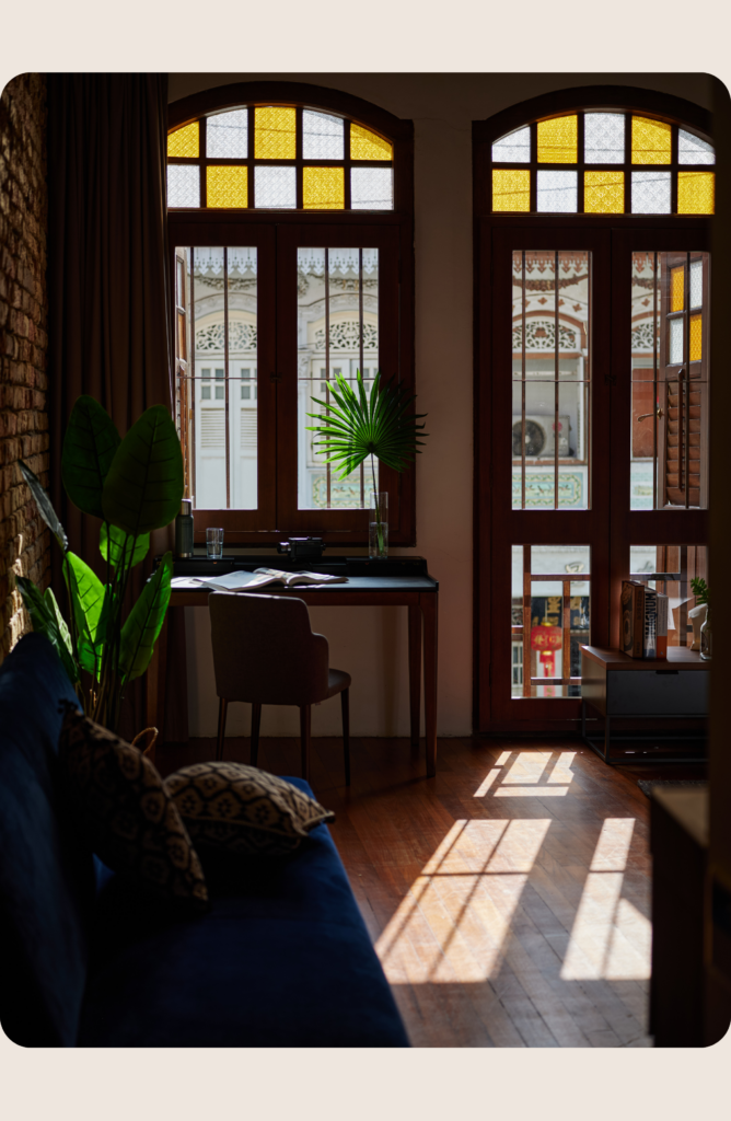 Sunlit shophouse interior with timber windows and workspace, illustrating coliving in Singapore through heritage stays and thoughtful design.