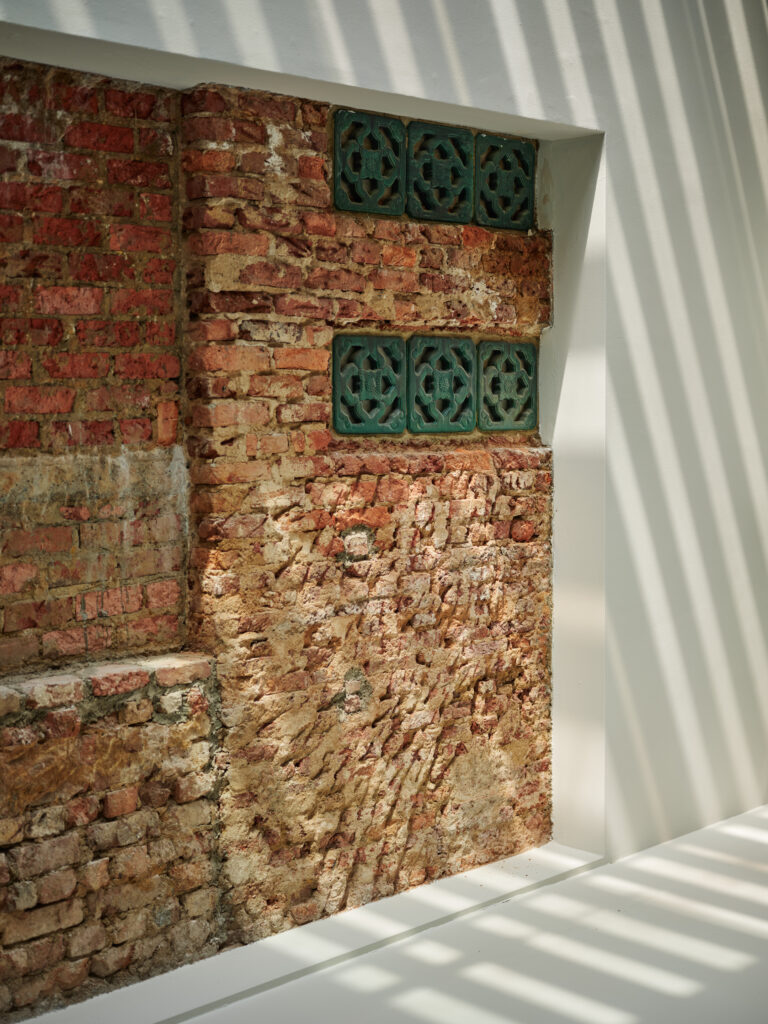 Exposed brick wall and vintage ventilation tiles inside a restored heritage home in Singapore, with soft daylight casting patterned shadows across the textured surface