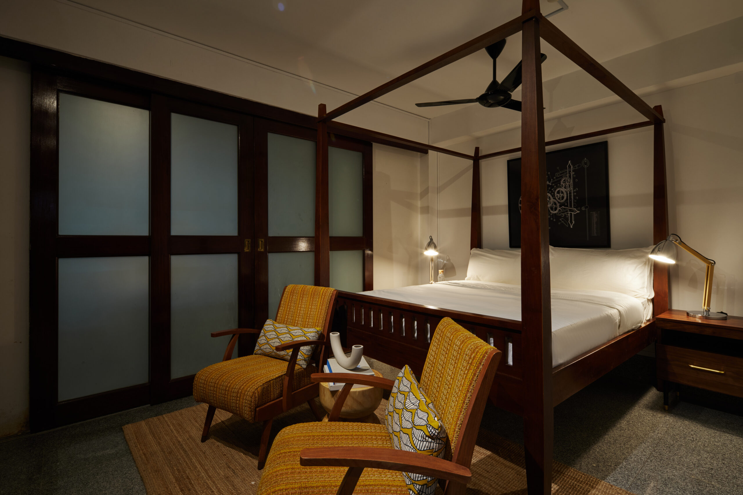 Bedroom featuring a dark wood canopy bed and two mid-century lounge chairs.